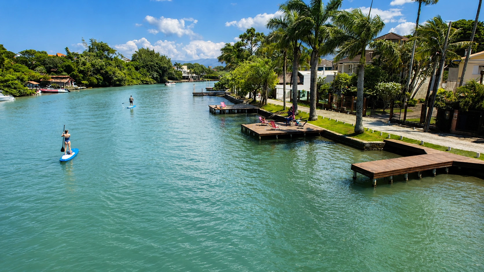 Canal da Barra da Lagoa cercado por vegetação, com pessoas praticando stand-up paddle
